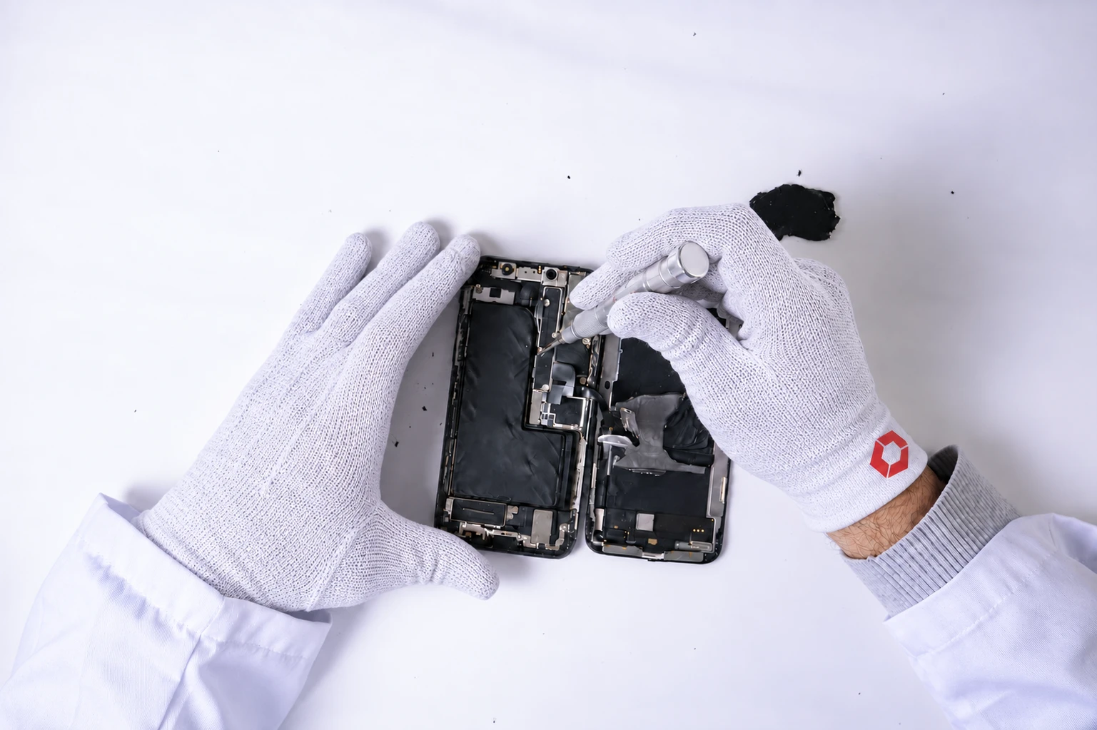 Techniker mit weißen ESD-Handschuhen öffnet ein Smartphone mit einem Präzisionsschraubendreher