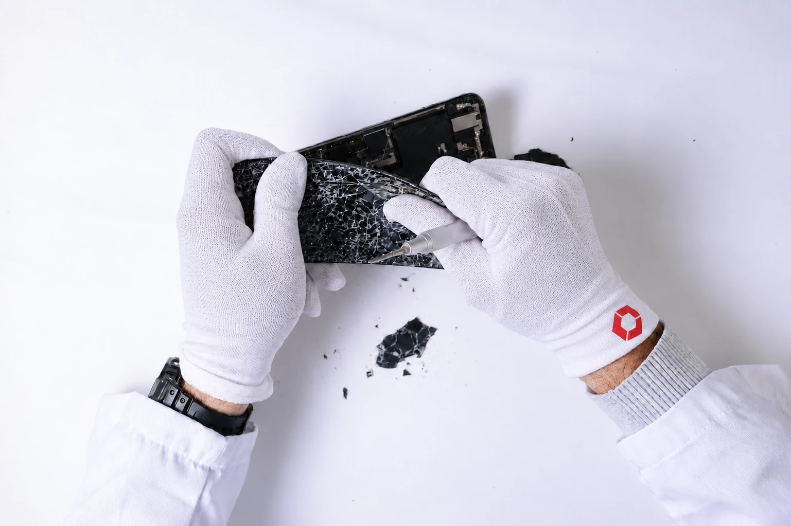 Techniker mit weißen ESD-Handschuhen löst gesprungenes Displayglas mit einem Präzisionswerkzeug